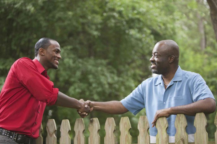 two neighbors shake across a fence